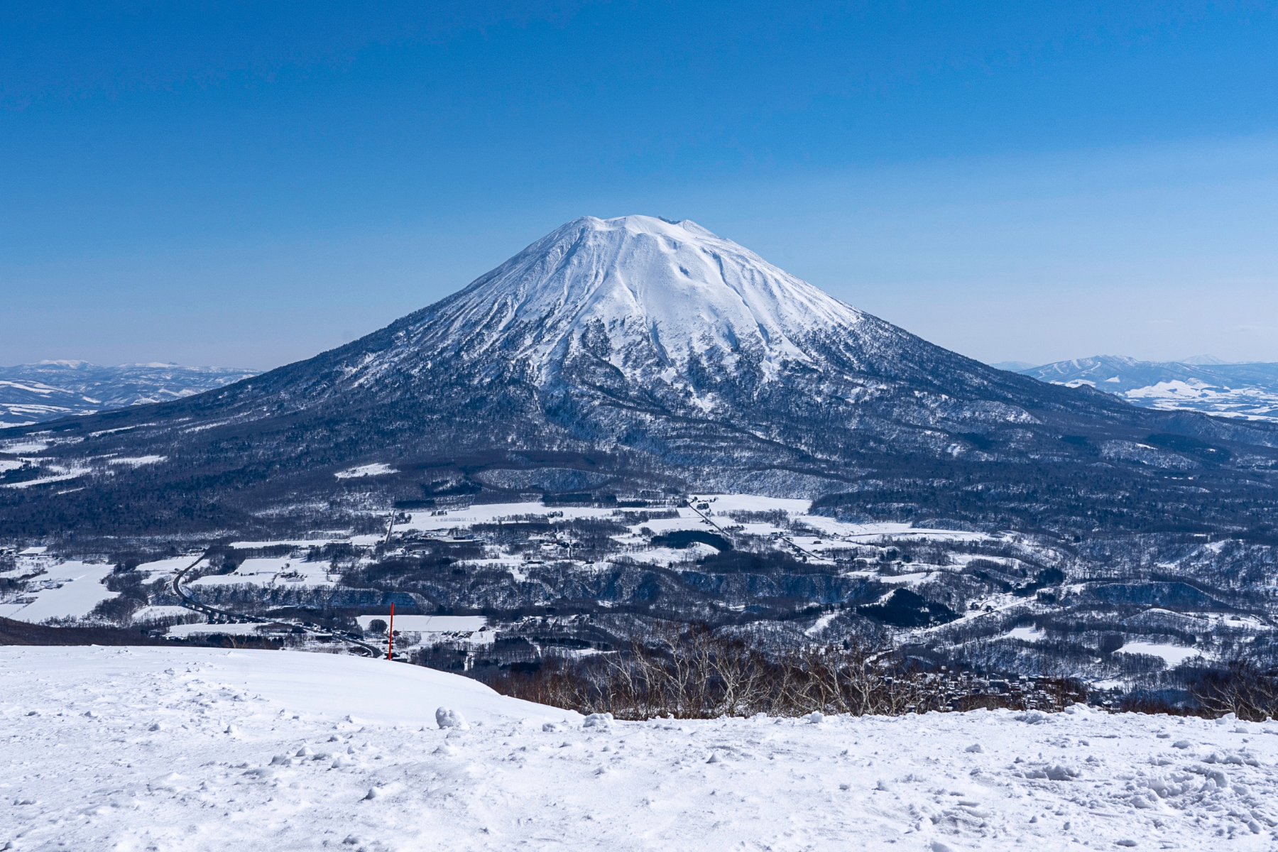 HOK-COVER-01 · a long straight road through Hokkaido snowfields, a lone figure far ahead — 3:2