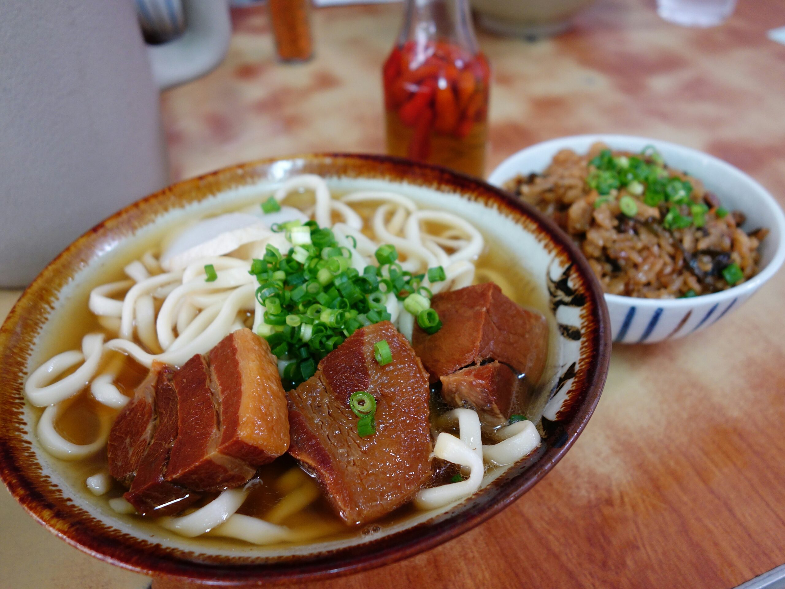 OKI-EAT-01 · Okinawa soba in a plain shop, chopsticks, laminated table. Documentary, not luxury. 3:2, 1800×1200