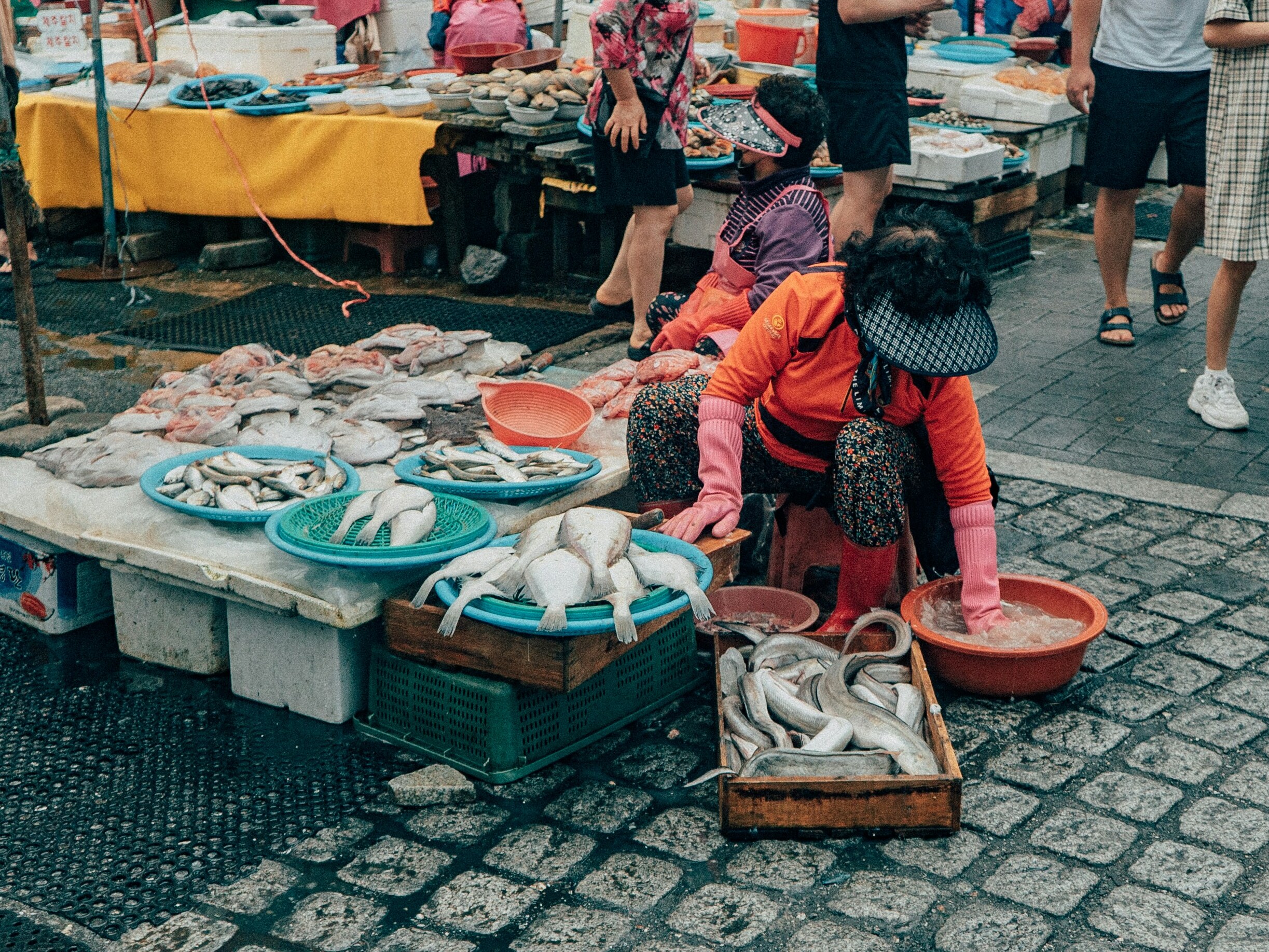 BS-MARKET-01 · dominant image — inside a busy seafood market, tanks and tables, vendors and buyers in motion. 3:2, 2000×1333