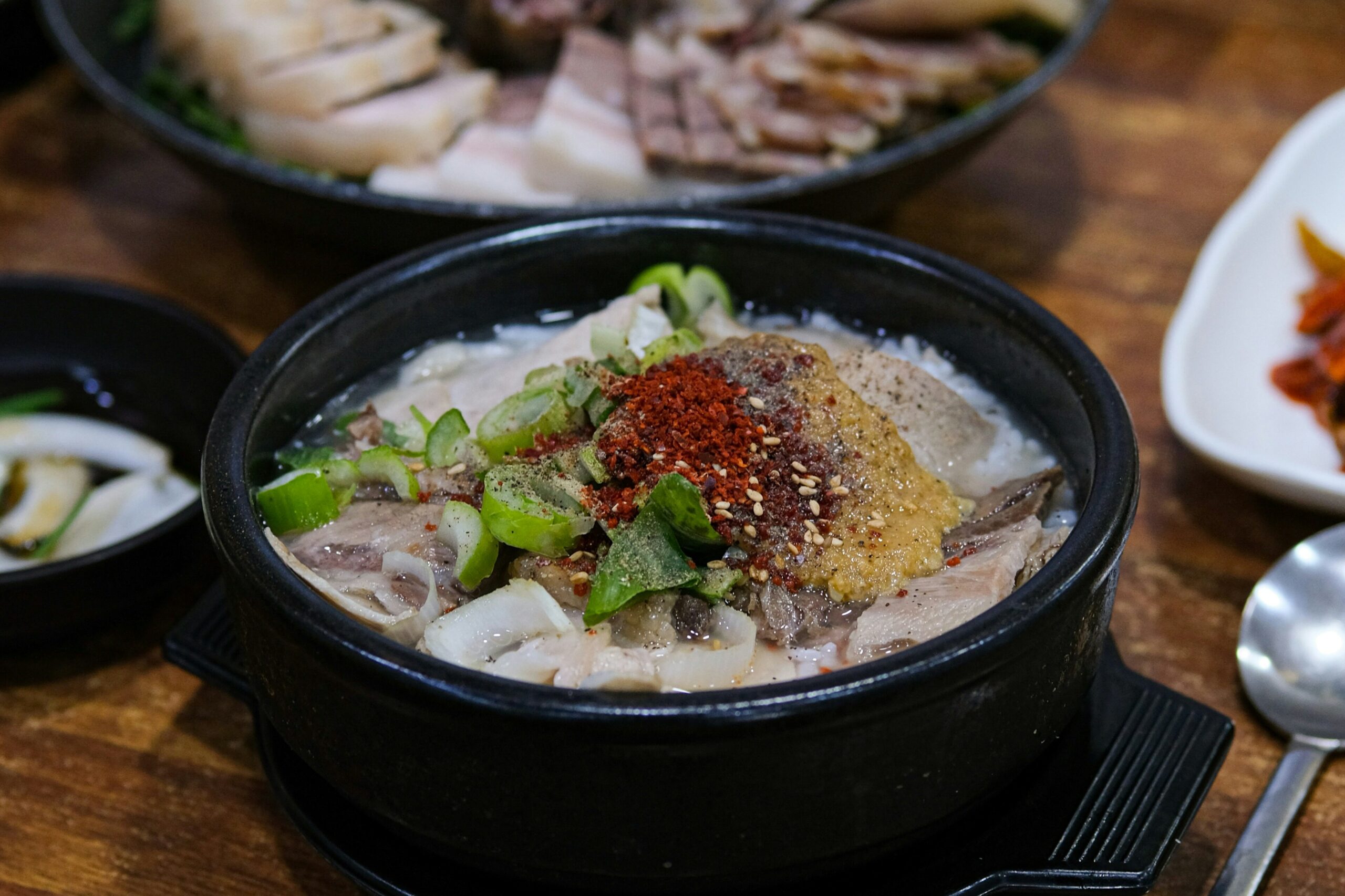 BS-EAT-03 · dwaeji-gukbap on a worn table, side dishes, close and tactile. 3:2, 1800×1200